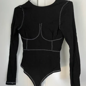 Frän, svart body med kontraststygn från Nelly - En redigt frän body från Nelly med kontraststygn som ger markerade drag. Låg i ryggen och stringmodell, säljer då den inte kommer till användning eller riktigt är min stil! Strl S och i väldigt gott skick. Säljer för 90 kr, fraktkostnad tillkommer!