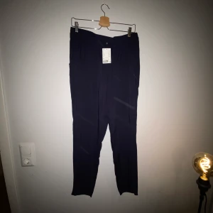 Tunna mörkblå finbyxor stl 44 - Tunna, mörkblå finbyxor med resår i midjan i stl 44 från H&M. Helt nya, prislappen sitter kvar. Kommer från djur- och rökfritt hem. Frakt tillkommer!