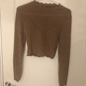 Stickad tröja  - En brun/beige stickad tröja, detaljer på armar och hals, inte använd 