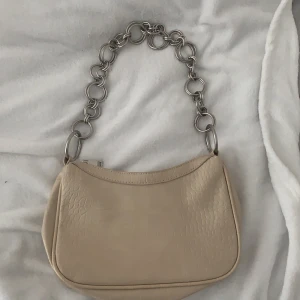 Beige bagusetteväska - Snygg väska med mönster och kedja från Nelly, säljs pga dålig användning (aldrig använd) nypris 349 säljs för 100 plus frakt ca 60 kr
