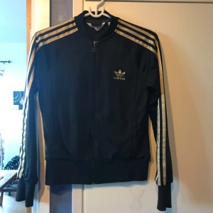  - Adidas tröja i använt skick, svart med guldiga detaljer. Frakten går på 45kr som köparen står för! 