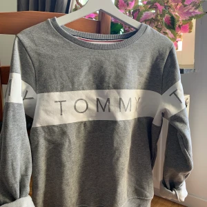 Tommy Hilfiger sweatshirt - Grå sweatshirt från Tommy Hilfiger med snyggt tryck på både fram- och baksida. Säljer pga att den tyvärr har blivit för liten! Väldigt mysigt material på insida vilket gör den perfekt för höst/vinterväder! NYPRIS: 899kr 