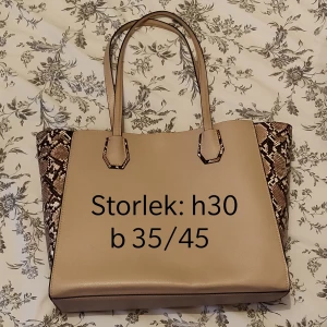 Större väska - Större väska i beige med ormskinns mönster på sidorna. Väskan är 30 cm hög och 35 cm nertill och 45 cm upptill på bredden. Det finns två öppna fack på insidan och ett med dragkedja. 😊 Kika gärna in vad mer jag säljer! 💞