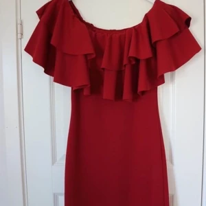 Klänning med volanger - Säljer en vinröd, thight klänning med två lager volanger upptill. Man kan antigen bära som off-shoulder klänning eller dra upp över axlarna. Aldrig använd!  Storlek: S/M