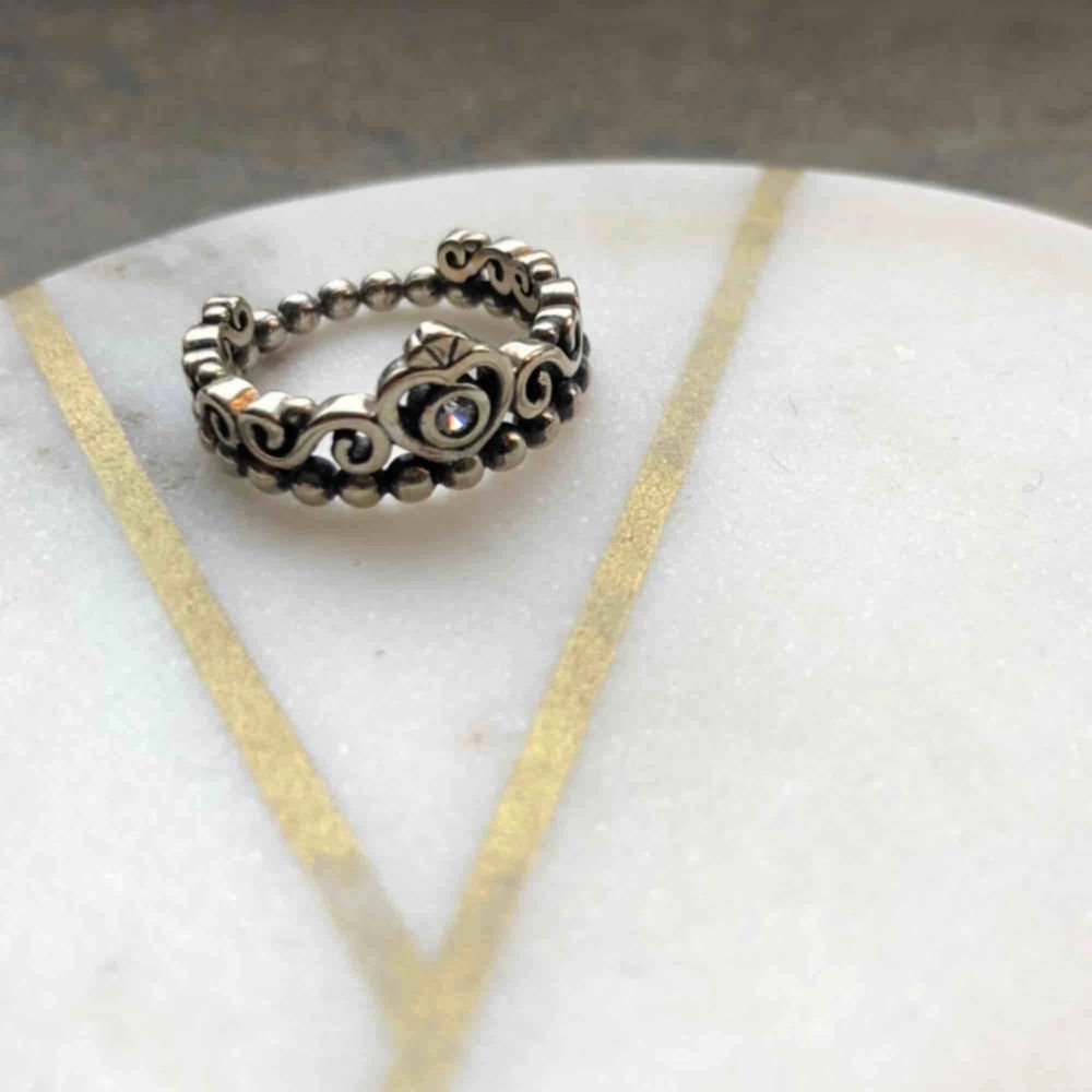 Ring formad som en krona 👑 Otroligt lik ’Pandora Tiara Ring’ men tror tyvärr inte den är äkta, därav priset💛  Ringen är mörkt silverfärgad med en liten vit sten i mitten, superfin! Diametern uppmätt till 1,8cm.   Endast använd enstaka gång. Frakt 11kr⭐️. Accessoarer.