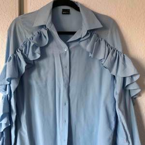 En härlig ljusblå skjorta med volanger på både ärmarna. Kan mötas upp i Lidköping. Köpare står för frakt. 