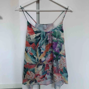  - Spagettiband’s linne med blommigt mönster. Aldrig använd. Frakt 18 kr