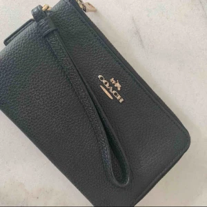  - Plånbok från Coach i svart med gulddetaljer för kort, kontanter och telefon (rymmer alla storlekar på iPhone) 2 fack med dradkedjor och en handledsrem