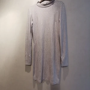 Tight, grå och långärmad festklänning - En grå klänning med silver "pluttar" (de sticker ut från tyget) över hela klänningen. Kan ej se att någon har trillat av. Hög i halsen och långärmad. Strechigt tyg. 