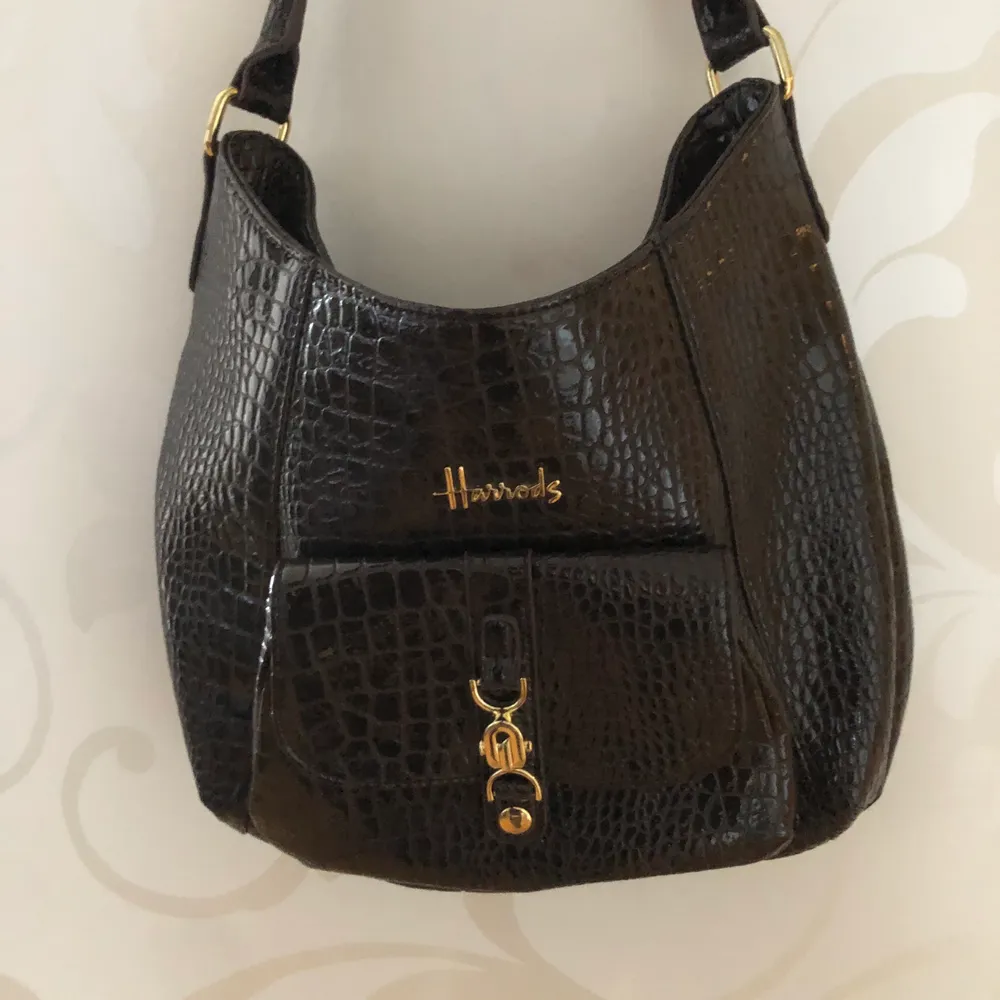 Glansig mörkbrun väska med gulddetaljer från Harrods💕  krokodilimitation! Knappt använd och bra skick. Väskor.