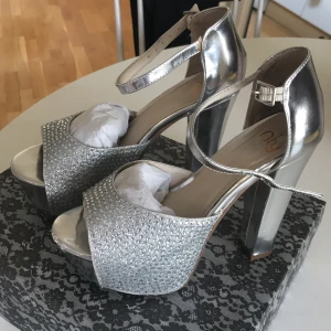 Silvriga klackar - Silvriga klackar från Nly. 14 cm klack och 4 cm platå. Använda en gång. Lite slitna framtill på vänstra skon.