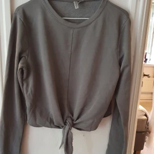 Grå sweatshirt med knytning - Grå sweatshirt med knytning fram. Även en söm-detalj fram. Köpt för några år sen på H&M men inte särskilt använd. Bra skick! ⭐ Storlek M. Säljs då den inte används. Kontakta vid frågor/intresse 💜 frakt inräknad