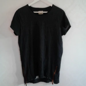  - Mörkgrå tshirt från Suit Apparel, använd en hel del men ändå i bra skick, finns nått enstaka små hål. Därav priset. Dragkedjor i koppar längst ner på varsin sida. Pris 40kr, kan skickas om köparen står för frakt!