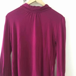  - Långärmad topp i fuschia från Mango Basics. Elegant med tre knappar och en öppning i nacken på mellanhög krage. 