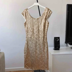  - Snygg guld-glittrande klänning täckt i paljetter men med mjukt tyg inuti. Den går ner lite i ryggen (se bild 2). (Frakt tillkommer om den ska skickas)