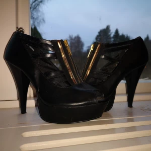 Klackskor med platå från din sko stl 37 - Bekväma och stabila klackar från din sko. Svart fakeläder med dragkedja och detaljer i guld. Platå 3 cm, klack 12 cm. Stl 37.