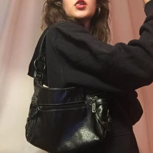 Svart väska  - En snygg väska som är köpt på secondhand, sitter super snyggt över axeln! Har massa fickor och spänen. Den e fint skick inga fläkar eller sönder någon stans!💋