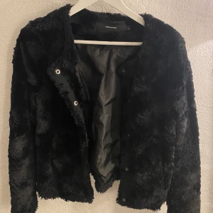 Kort Fuskpäls Jacka - Kort svart fuskpäls jacka med mjukt material och tryckknappsstängning. Använd under en sommar men inget mer. Ordinarie pris: 399,95kr