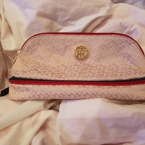 Tommy Hilfiger necessär   - Rosa satin necessär med skinnbotten,  röd/blå dragkedjor med skinndetaljer.  Oanvänd med plast kvar på guldemblem. Två fack, varav ett i botten som passar perfekt för tandborsten och andra platta saker, samt ett stort för alla resterande prylar. 