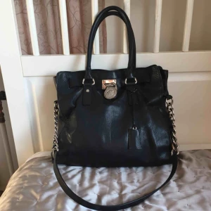  - Väska i skinn från Michael Kors. Den är använd och något sliten. Skinnet på ena kortsidan har en mindre skada och fodret har några mindre fläckar från bläck och läppstift (syns dock inte så mycket). Har fler bilder!