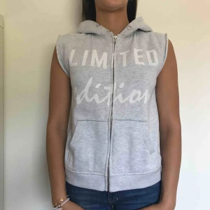  - En grå luvtröja med dragkedja utan ärm. Har ett vitt tryck på bröstet där det står limited edition. Är lite sliten vid kragen vilket syns på bild nr 3. Kostar 150kr inklusive frakt.