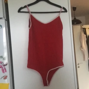 Röd body stl s - Röd body med vita detaljer. Öppnas i grenen. 