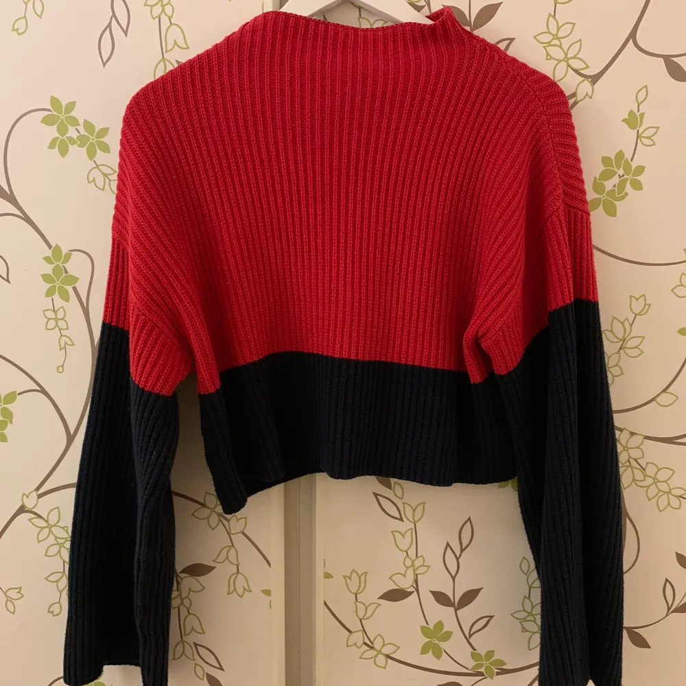 Stickad och croppad tröja i rött och mörkblått (ser typ svart ut) med ståkrage och lite vidare ärmar. Använd en del men inte alls sliten. . Stickat.