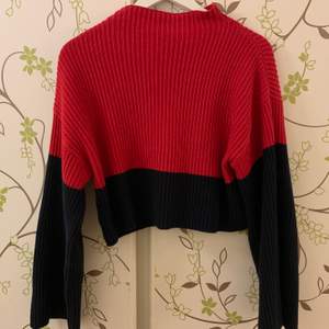 Stickad och croppad tröja i rött och mörkblått (ser typ svart ut) med ståkrage och lite vidare ärmar. Använd en del men inte alls sliten. 