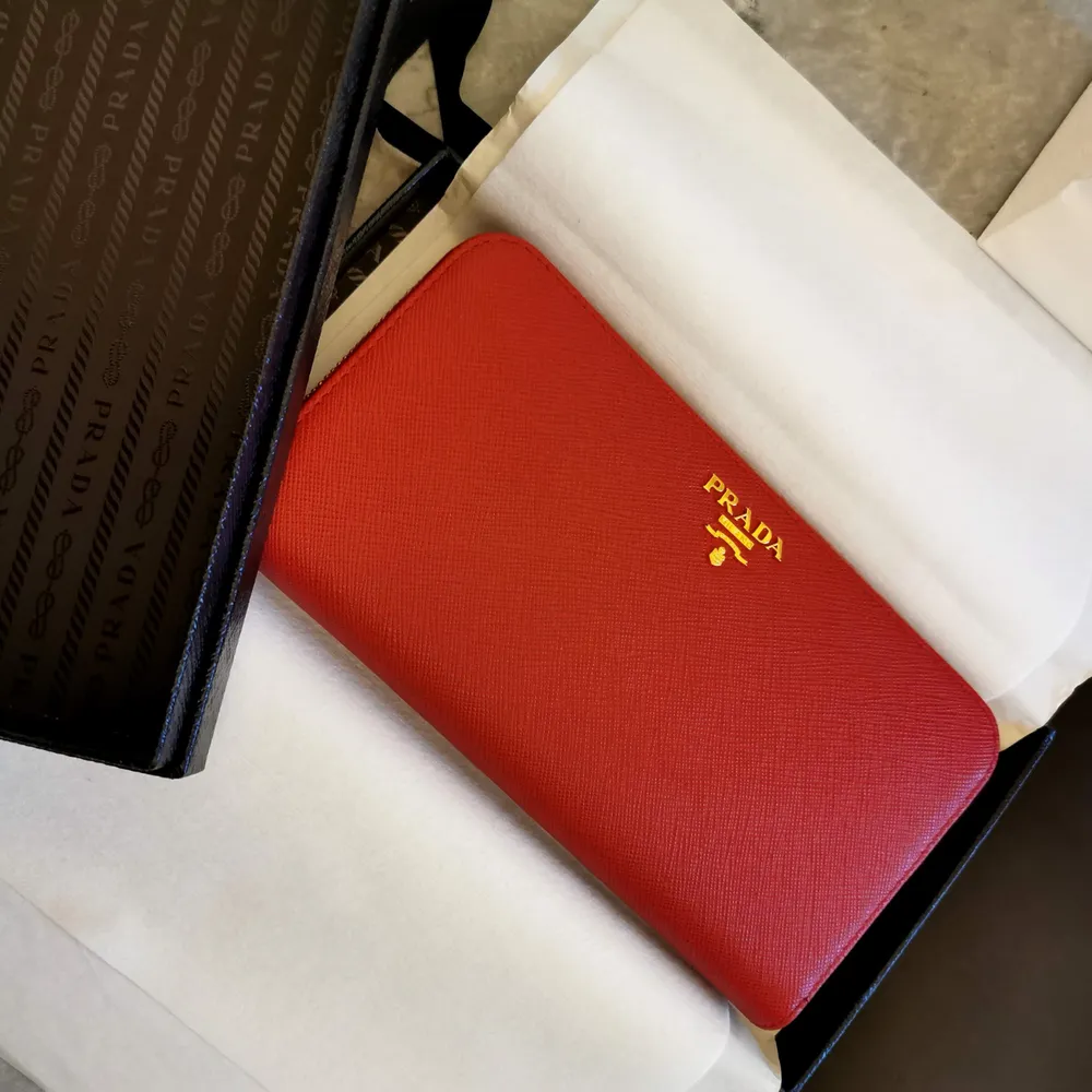 Hel ny och oanvänd plånbok från Prada i den lyxiga färgen röd.  Det är en gåva som aldrig har kommit till användning och endast legat nedpackad i sin kartong.  Inköpt på Prada birger jarlsgatan i Stockholm.  Kvitto, presentkartong, snöre, papper och påse . Accessoarer.