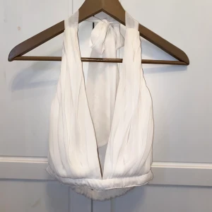 Vit croptop/festtopp - Supersnygg vit croptop med djup urringning som knyts bak i nacken. Jättefint polyesterliknande blustygsmaterial. Justerbar storlek pga stretchmaterial i bandet baktill samt knytfunktion i nacken.  Kampanj: KÖP 3 BETALA FÖR 2