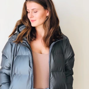 Metallic charcoal puffy coat by Rains - The Puffer jacket by Rains speaks for itself. Signature silhouette, casual fit, comes in a metallic charcoal color. Super warm, waterproof and windproof, has a hood, hem at the hips.