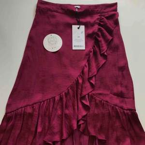 Satin wrap over kjol från NA-KD. Kjolen är endast testad och därmed som ny.  Material: Satin Färg: Lila/rosa/vinröd (Burgundy)  (frakt tillkommer)