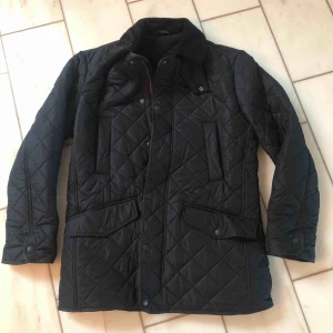  - Oanvänd quiltad mörkblå Barbour jacka i storlek S. Innerfoder i fleece. Rak modell och därför stor i storleken, passar den som vanligtvis bär storlek M. Aldrig använd, perfekt skick