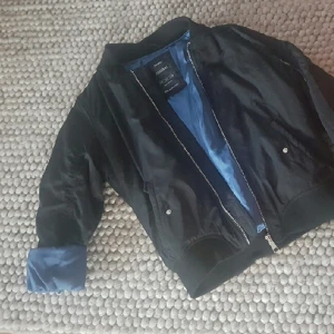  - Säljer en knappt använd bombarjacka som köptes i somras i Barcelona. Svart bombarjacka i storlek 36-38, silverdetaljer med blå insida.