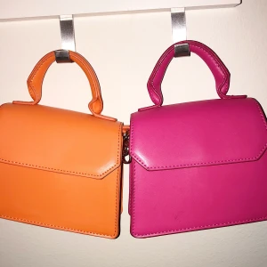 Rosa och orange axelremsväska från Ginatricot  - Säljer dessa två välskor tillsammans som ett sett för 110kr, ifall man vill köpa en så kostar dom 70kr styck. Super fina och oanvända då jag har använder dom som prydnad. Köpte dom för 280kr styck. De är slutsålda på hemsidan och måtten är: 16*13, de går att bära i både handtaget och axelremmen💓💓