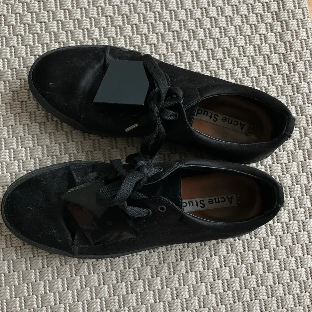 Svarta sneakers från Acne Studios i silkigt material och med den klassiska loggan!  Så snygga skor men har för många svarta så hoppas någon annan får mer användning av dem.  De är använda men fortfarande sjukt fina, fråga för mer bilder 🥰. Skor.