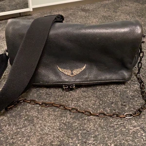 Zadig&Voltaire  - Säljer denna fina väska ifrån Zadig&Voltaire. Den är i svart läder och det tillkommer ett band och en kedja. Säljer då jag inte använder den längre. Kedjan har tappat lite färg men annars är väskan i rätt bra skick. Inköpt på zadig butiken i Stockholm på birger Jarlsgatan 8. Nypris: 395€ ca 4000kr 