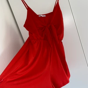 Playsuit röd Stl M - Väldigt fin röd playsuit från lefties. Stretchig storlek M passar S-L. Perfekt till stranden eller fest. Använd 2 gånger. Dressen har en Knut som du kan knyta om. 