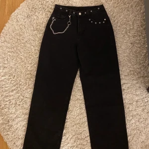 Svarta jeans - Svarta jeans med snygga detaljer. Avtagbar kedja. Helt oanvända och säljs då de är för stora. Passar S-M beroende på hur man vill att de ska sitta.