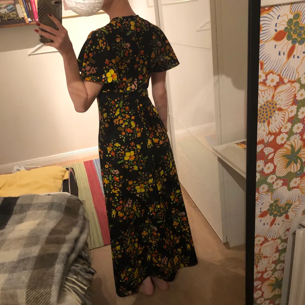 Säljer min fantastiskt vackra långklänning från 70-talet med blommor i klassiska 60-70talsfärger! På bröstet finns det en snörning som går att knyta, själv har jag även valt att vika in snörningen för att få en mer rundad urringning. Mjukt och härligt tyg, jag är 170cm lång och är oftast en small!🧡💚💛. Klänningar.