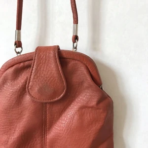  - Brunröd liten väska i fejkskinn från med långt axelband jag knutit upp. Fint innerfoder med liten ficka. Bruksskick, men kvar att ge!    Kan mötas i Stockholm eller skickas mot fraktkostnad! ✨🌸✨