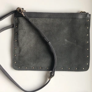 Crossbody väska  - En tunn crossbody väska, med avtagbara band. Används även som nescesär eller fodral till iPad mini. Yttre fickan är i ”sammetsliknande material” 
