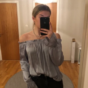Offshoulder blus - Jättefin silver/grå offshoulder blus från Gina tricot. Den har ett snöre som detalj som man kan styla på olika sätt samt resår vid slutet av ärmarna. Bra skick. Frakt ingår i priset.