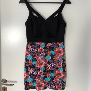 Klänning i svart, mesh och blommor - Klänning från Bebes märke 2B. Svart, mesh och blommönster. Cutouts ovanför urringningen vid axelbanden. Ev av mina favoriter, använt men i bra skick. Dags för en annan ägare. 