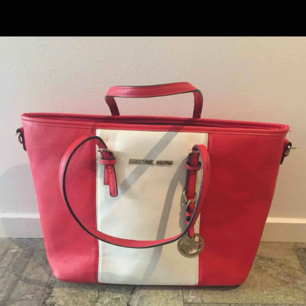 Vit och röd randig Michael Kors väska i relativt bra skick. OBS, trasig dragkedja på facket på backsidan av väskan. Köptes för: 500kr. Accessoarer.