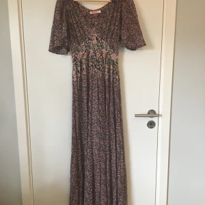 Blommig klänning från Indiska - Blommigt mönstrad klänning från Indiska. Stl XS, ganska stor i storlek. Gott skick, knappt använd. Frakt betalas av köparen.