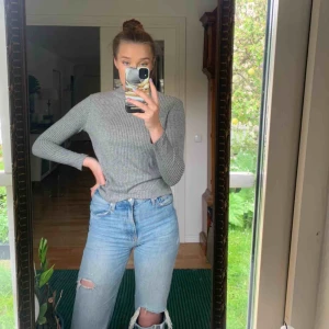  - En grå, ribbad, långärmad tröja som är lite upphöjd i halsen. 