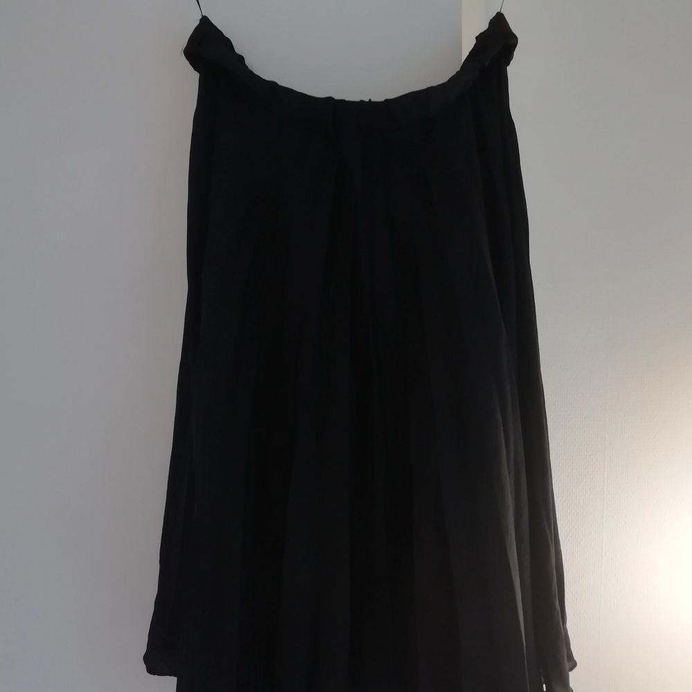 Vågig svart kjol i glansigt tyg . Kjolar.