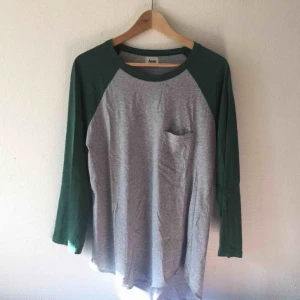  - Grå/grön långärmad t-shirt från Acne. ”Baseball” modell i storlek Medium. Något länge bak (se bild). Finns ett litet hål nere i högra kanten - går enkelt att laga!  