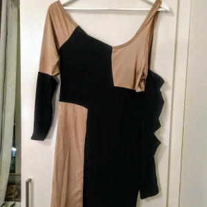  - En klänning i ljust brun och svart med öppning vid armhålorna och bara axlar. Använd 1 gång, fint begagnat skick. Sitter som en M.